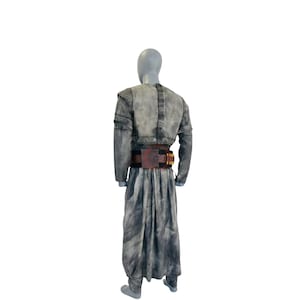 Puede incluir: Un conjunto de t&uacute;nica de manga larga y falda larga a juego con un acabado gris moteado y desgastado. El atuendo incluye un cintur&oacute;n utilitario de color marr&oacute;n oscuro en la cintura, decorado con una hebilla rectangular y trabillas doradas.