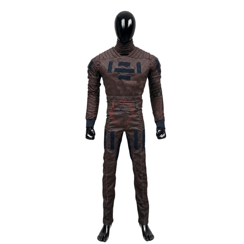Puede incluir: Un mono de cuerpo entero marr&oacute;n sobre un maniqu&iacute; negro, con cuello alto, detalles acolchados en los hombros y parches rectangulares oscuros en el pecho y los muslos. La prenda tiene mangas largas con pu&ntilde;os oscuros y una cintura ajustada.