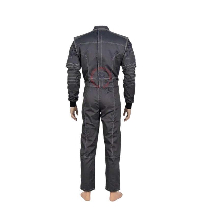 May include: A dark gray racing suit featuring long sleeves with black ribbed cuffs, a high collar, and prominent white contrast stitching throughout the garment. The back of the suit displays a circular red logo graphic centered on the upper back area.