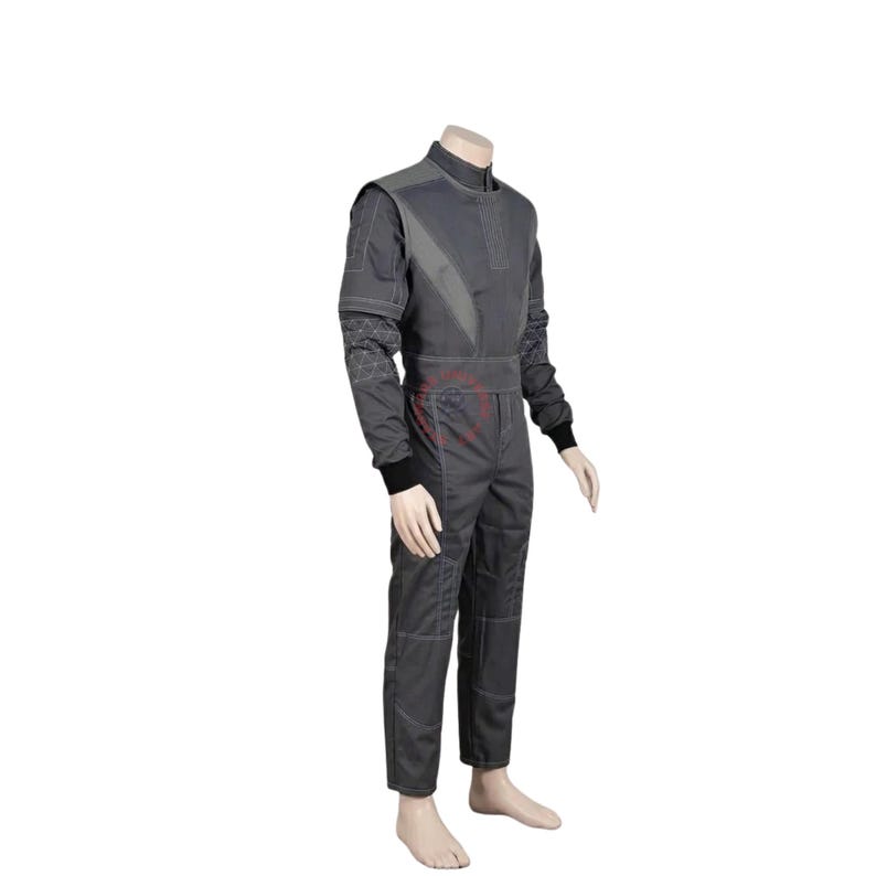 May include: A dark gray long-sleeved jumpsuit featuring a high collar, a structured bodice with diagonal paneling, and black ribbed cuffs at the wrists. The garment includes visible white stitching details along the seams and a red circular logo.