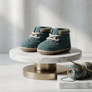 Peut inclure: Une paire de chaussons pour bébé en crochet bleu sarcelle avec une bordure beige le long de la semelle et du col, dotés de lacets couleur crème noués. Les chaussons présentent un motif en maille texturée et une forme montante arrondie.