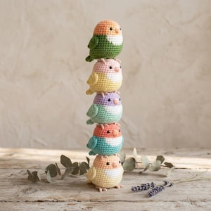 May include: A vertical stack of five crocheted bird figurines. Each bird features a two-tone color scheme with a white chest and black bead eyes. The colors include peach and green, pink and yellow, lavender and mint, coral and teal, and peach and yellow.