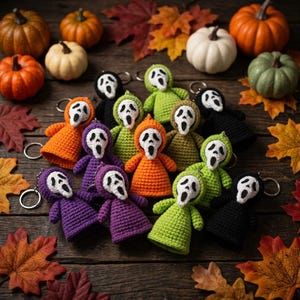 May include: A collection of crochet keychains shaped like ghost figures with white faces and black eye and mouth details. The figures wear hooded robes in orange, purple, lime green, olive green, and black, each attached to a metal keyring.