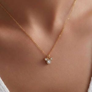 Puede incluir: Un delicado collar dorado con un colgante con un dise&ntilde;o de tres c&iacute;rculos, cada uno adornado con peque&ntilde;os cristales brillantes. El collar cuelga de una fina cadena dorada. El colgante tiene aproximadamente 1,3 cm de di&aacute;metro.