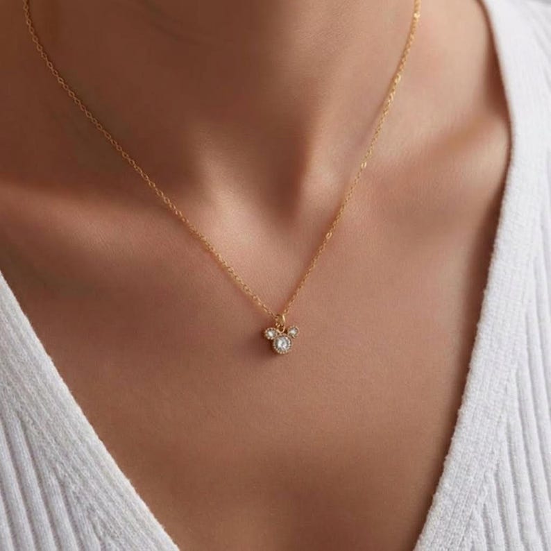 Puede incluir: Un delicado collar dorado con un colgante con un dise&ntilde;o de tres c&iacute;rculos, cada uno adornado con peque&ntilde;os cristales brillantes. El collar cuelga de una fina cadena dorada. El colgante tiene aproximadamente 1,3 cm de di&aacute;metro.