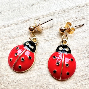May include: A pair of ladybird earrings. Each earring features a red body with black spots and a black head. The earrings have gold-coloured posts and accents.