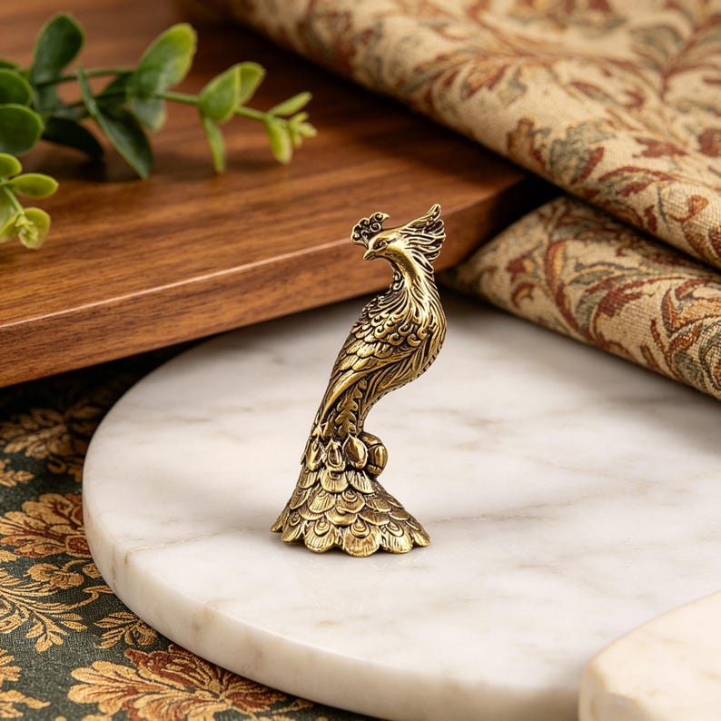 Puede incluir: Una peque&ntilde;a figura de metal de color dorado que representa un pavo real de pie. El ave presenta detalles intrincados de plumas en relieve en todo el cuerpo y una base en forma de abanico. La superficie tiene un acabado pulido de estilo antiguo.