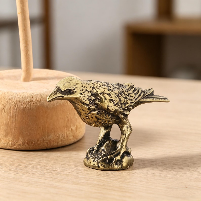 May include: A detailed brass bird figurine with textured feathers and a detailed beak. The bird is perched on a textured base, showcasing a vintage aesthetic. The figurine is a decorative item.