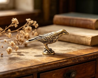 May include: A detailed brass bird figurine with textured feathers and a small, round base. The bird is perched on a wooden surface, with dried flowers and antique books in the background. The figurine is a decorative item.