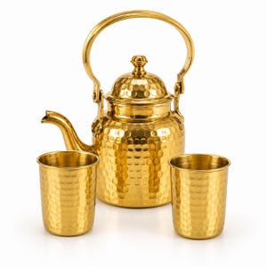 May include: A gold-colored metal tea set consisting of a hammered-texture teapot with a curved spout, a lid with a small knob, and a hinged handle, accompanied by two matching hammered-texture metal cups with a cylindrical shape and smooth rims.