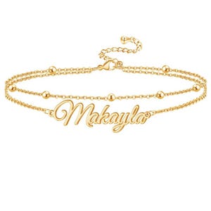 May include: A gold-toned double-chain anklet featuring a central nameplate with the script text Makayla. The delicate chain is accented with small, evenly spaced gold beads and includes a lobster claw clasp at the end of the extension chain.