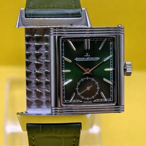 May include: A rectangular Jaeger-LeCoultre watch with a green dial, silver-tone hands and hour markers, and a small seconds sub-dial. The watch features a silver-tone case with a textured metal side and a green leather strap with a crocodile pattern.