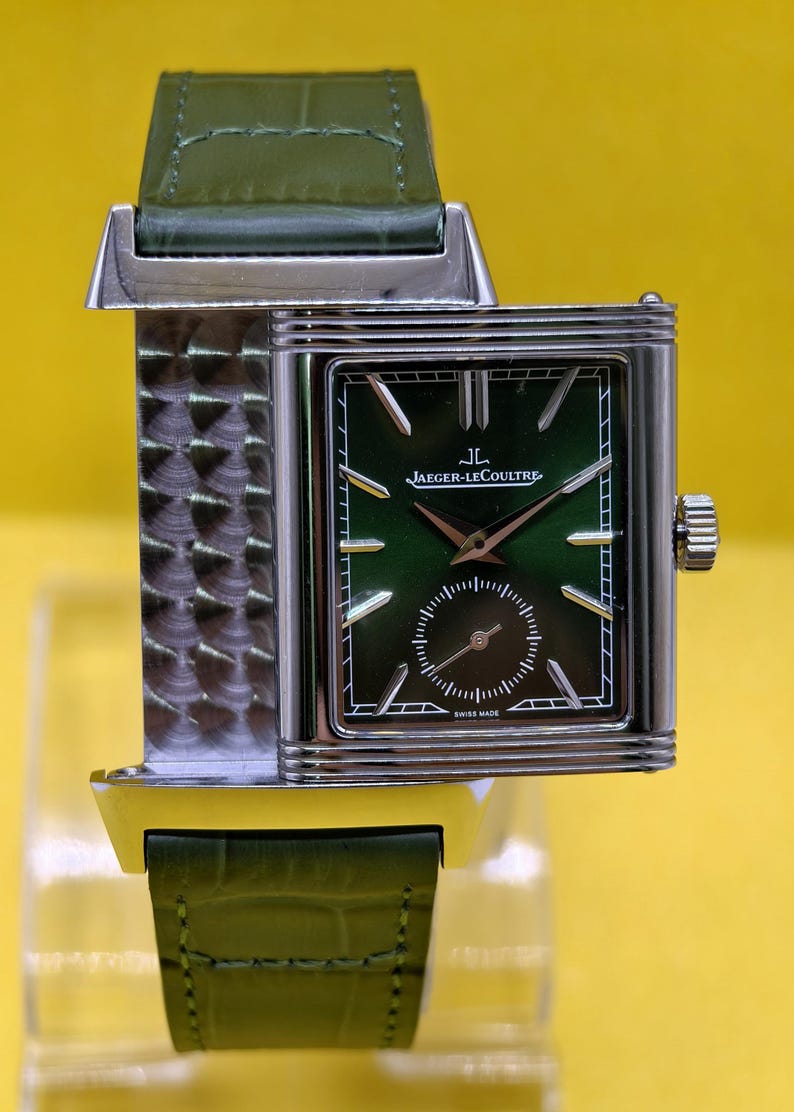 May include: A rectangular Jaeger-LeCoultre watch with a green dial, silver-tone hands and hour markers, and a small seconds sub-dial. The watch features a silver-tone case with a textured metal side and a green leather strap with a crocodile pattern.