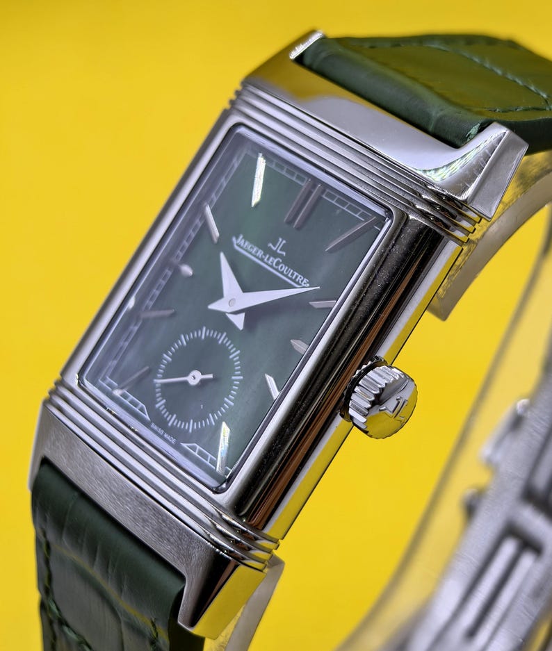 May include: A rectangular silver-tone wristwatch with a dark green dial, silver hands, and silver hour markers. The watch features a small seconds sub-dial at the bottom, the Jaeger-LeCoultre logo, and a dark green leather strap with a textured finish.