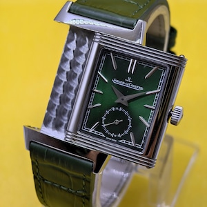 May include: A rectangular silver-tone wristwatch with a green sunray dial, silver hands, and indices. The watch features a small seconds sub-dial, the text Jaeger-LeCoultre, and a green alligator-textured leather strap with a metallic side panel.