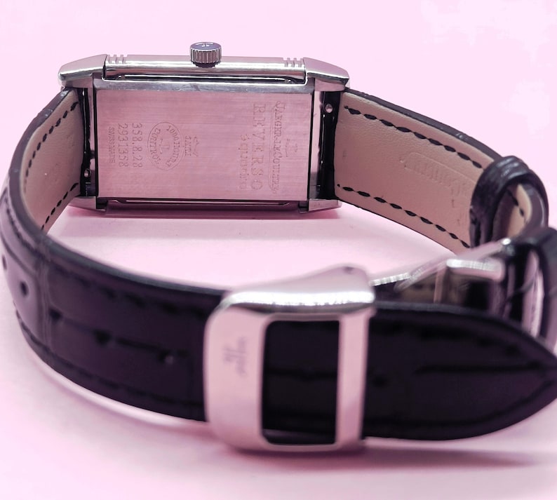 Pu&ograve; includere: Un orologio da polso rettangolare argentato con cinturino in pelle nera. Il quadrante dell'orologio non &egrave; visibile, ma il retro dell'orologio presenta testo e numeri incisi. Il cinturino &egrave; fissato con una chiusura argentata.