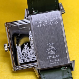 May include: A rectangular Jaeger-LeCoultre Reverso watch with a green leather strap. The case back features an engraving of the Palace of Westminster and Big Ben. Text includes JAEGER-LECOULTRE, REVERSO, 3 bar, 1000 HOURS CONTROL, 277.8.62, 2837765, SWISS MADE.