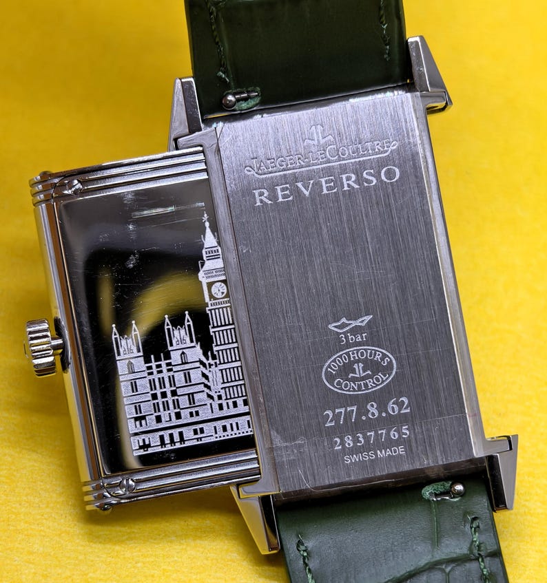 May include: A rectangular Jaeger-LeCoultre Reverso watch with a green leather strap. The case back features an engraving of the Palace of Westminster and Big Ben. Text includes JAEGER-LECOULTRE, REVERSO, 3 bar, 1000 HOURS CONTROL, 277.8.62, 2837765, SWISS MADE.