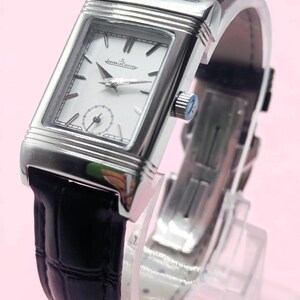 Pu&ograve; includere: Un orologio da polso rettangolare argentato con quadrante bianco e cinturino in pelle nera. L'orologio presenta un piccolo quadrante dei secondi e il marchio "Jaeger-LeCoultre". Il cinturino &egrave; nero e l'orologio &egrave; esposto su un supporto trasparente.
