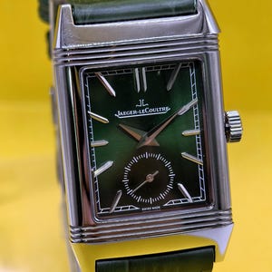 May include: A rectangular silver-tone wristwatch featuring a green gradient dial with silver hour markers, a small seconds sub-dial, and the text Jaeger-LeCoultre and Swiss Made. The watch has a green leather strap with a textured crocodile pattern.