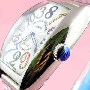 May include: A silver wristwatch with a white face featuring colorful numerals and hands. The watch face displays the text "FRANCK MULLER GENEVE" and "CRAZY COLOR DREAMS". The watch has a blue crown.