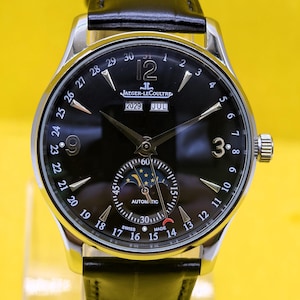 May include: A silver-tone automatic wristwatch with a black dial, featuring a moon phase sub-dial, a date indicator ring numbered 1 to 31, and a black leather strap. The dial displays the text Jaeger-LeCoultre, 2029, JUL, Automatic, and Swiss Made.