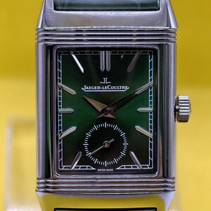 May include: A rectangular silver-tone watch with a green dial and a green leather strap. The dial features the text JAEGER-LECOULTRE and SWISS MADE, with silver-tone hour markers, a small seconds sub-dial, and a crown on the right side of the case.