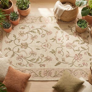 May include: A rectangular area rug featuring a cream-colored base with a symmetrical floral pattern in muted pink and sage green. The design includes scrolling vines and blossoms, framed by a decorative border with matching botanical motifs.