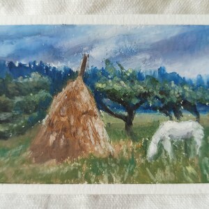 May include: A rectangular painting on paper depicting a rural landscape with a large brown haystack in the center, a white horse grazing in the green grass to the right, and dark green trees under a cloudy blue sky with visible brushstrokes.