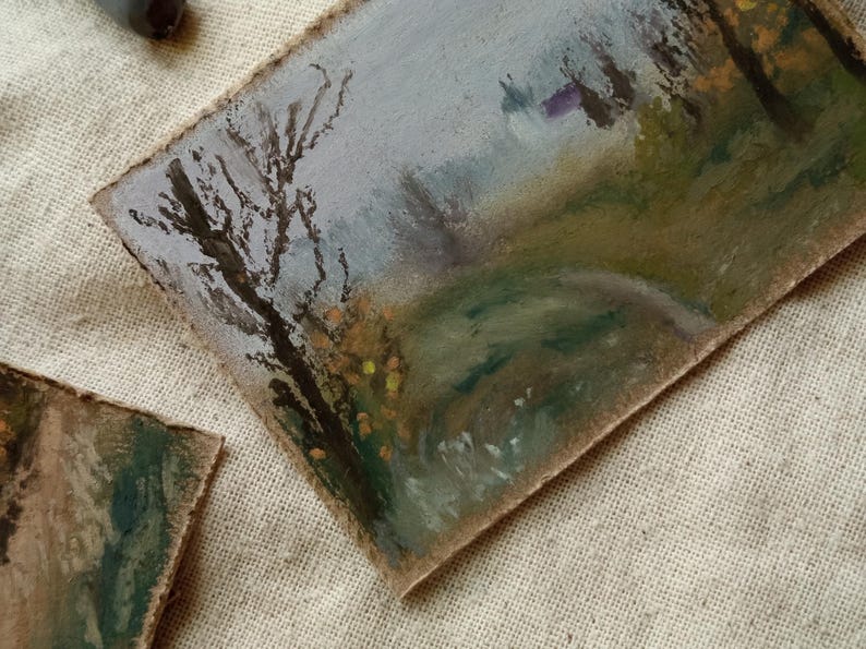 May include: Oil pastel landscape painting on textured paper. The artwork depicts a path winding through a misty forest, with a bare tree in the foreground. The color palette includes muted greens, browns, and grays, with touches of yellow.