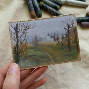 May include: A small, rectangular landscape painting featuring a path winding through a misty forest. The artwork uses pastel colors, with a focus on greens, yellows, and purples. Bare trees and a distant building are visible.