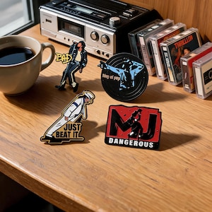 May include: Four enamel pins featuring Michael Jackson imagery: one labelled BAD, one labelled JUST BEAT IT, one circular pin with blue silhouette art, and one rectangular red and black pin labelled MJ DANGEROUS, arranged on a wooden surface.