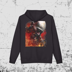 May include: A black hooded sweatshirt featuring a large rectangular graphic on the back. The print depicts a bald figure with a dark, weathered face surrounded by vibrant orange and red flames, with glowing embers scattered throughout the scene.