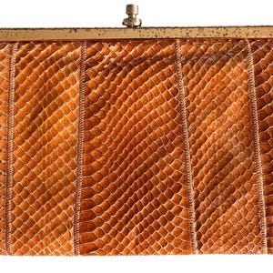May include: A vintage clutch purse with a snakeskin pattern in shades of brown and tan. The rectangular bag features vertical stitched panels and a gold-toned metal clasp.