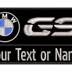Op de afbeelding: Een rechthoekige zwarte geborduurde patch met het wit-blauwe BMW-logo aan de linkerkant, de zilverkleurige letters GS aan de rechterkant en de tekst Your Text or Name geborduurd met wit garen langs het onderste gedeelte van de patch.