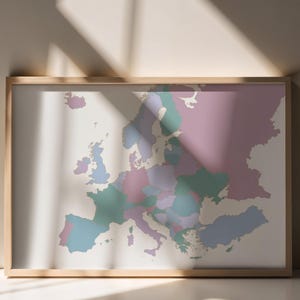 Puede incluir: Un mapa de Europa enmarcado que presenta una paleta de colores suaves con tonos rosa, azul verdoso y azul para cada país. El mapa se presenta en un marco de madera de tono claro con un diseño limpio, sencillo y minimalista.