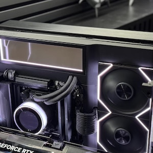 Pode incluir: O interior de um gabinete de computador preto com um sistema de refrigeração líquida, um bloco de bomba circular, duas ventoinhas iluminadas à direita e uma placa gráfica com o texto GEFORCE RTX, acentuado por faixas de luz LED brancas.