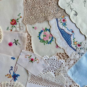 May include: A collection of vintage linens featuring white and cream fabric squares with colourful cross-stitch floral embroidery, intricate beige and white crochet lace doilies, and scalloped edges with delicate needlework patterns.