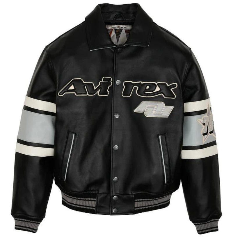 May include: Black leather jacket with white and gray accents on the sleeves. The jacket features the brand name "Avi'rex" in white lettering across the chest, along with a gray and white patch. The jacket has a ribbed collar and cuffs.