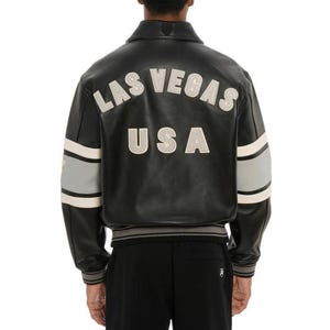 May include: Black leather jacket with the words "LAS VEGAS USA" in white lettering on the back. The jacket has gray and white stripes on the sleeves and a ribbed hem and cuffs. The jacket is a classic bomber style.