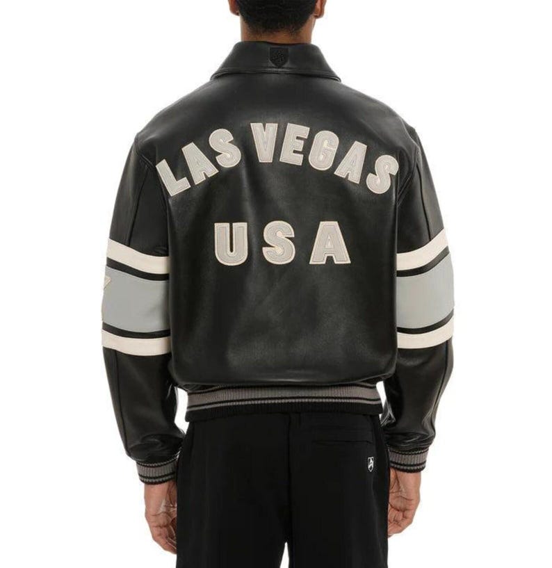 May include: Black leather jacket with the words "LAS VEGAS USA" in white lettering on the back. The jacket has gray and white stripes on the sleeves and a ribbed hem and cuffs. The jacket is a classic bomber style.