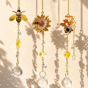 May include: Three decorative suncatchers with bee and honeycomb designs. Each suncatcher features a gold chain, yellow and clear crystal beads, and a large crystal ball. The bee suncatchers have yellow and black striped bees, and the honeycomb suncatcher has a gold honeycomb.