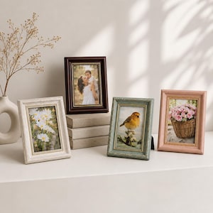 May include: Four decorative picture frames in various colors and styles. One frame is dark brown, another is light blue, a third is white, and the last is pink. Each frame holds a different image, including a photo of a person, flowers, and a bird.