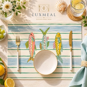 May include: A table setting featuring a placemat with a blue and white striped design and three fish illustrations. The setting includes a white plate, gold cutlery, and the text "LUXMEAL ELEVATE EVERY MEAL".