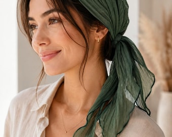 May include: A dark forest green headscarf made of a lightweight, semi-sheer, crinkled fabric. The square-shaped scarf is folded diagonally and tied securely at the back of the head, featuring a delicate lettuce-edge hem along the finished borders.
