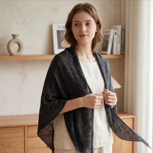 May include: A black and white striped shawl draped over a person. The shawl is made of a lightweight fabric with a subtle pattern. The person is wearing a white top.