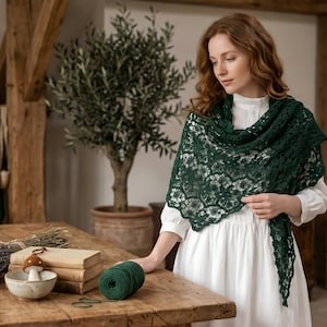 May include: A woman wearing a dark green lace shawl over a white dress. A wooden table displays books, dried lavender, and a ball of green yarn. An olive tree is in the background.