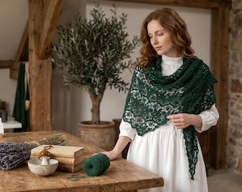 May include: A woman wearing a dark green lace shawl over a white dress. A wooden table displays books, dried lavender, and a ball of green yarn. An olive tree is in the background.