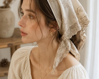 May include: A cream-colored headscarf featuring delicate floral embroidery and a scalloped lace trim along the edges. The fabric is lightweight and tied at the back, showcasing intricate needlework patterns across the surface of the textile.