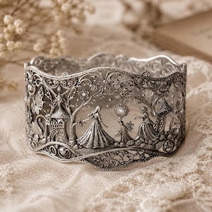 May include: A wide silver cuff bracelet featuring intricate filigree metalwork. The design depicts a detailed scene with figures in long dresses, a castle, trees, and a butterfly. The metal has a polished finish with dark recessed areas.